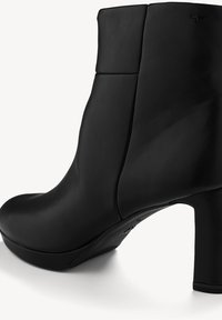 Bottine en cuir noir avec un bout arrondi, un talon épais, une texture lisse et un détail de couture minimaliste. Le panneau latéral présente une couture.