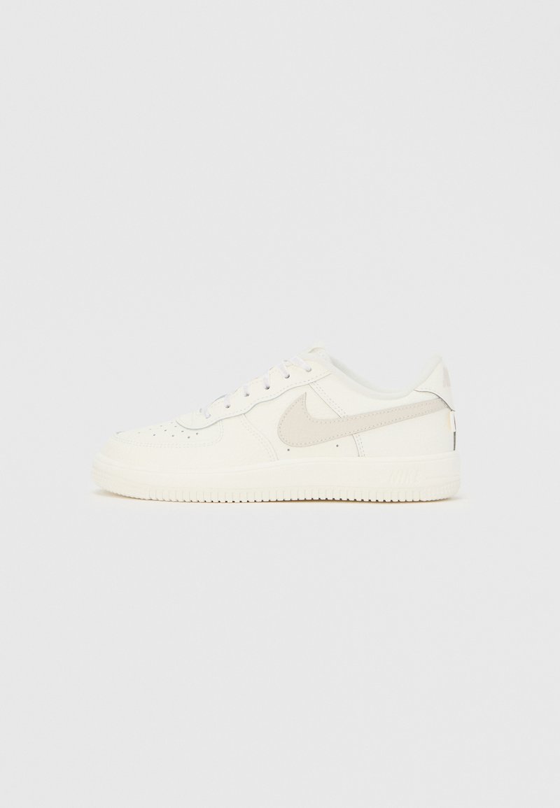 Λευκό αθλητικό παπούτσι Nike χαμηλού τύπου με ανοιχτό γκρι λογότυπο Swoosh, κλείσιμο με κορδόνια, διάτρητο κουτί δαχτύλων και υφή σόλας σε απλό φόντο.