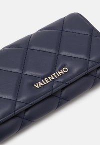 Jūras zila quiltota ādas maciņš ar zelta "Valentino" aparatūru, ar gludu tekstūru un dimanta rakstu uz virsmas.