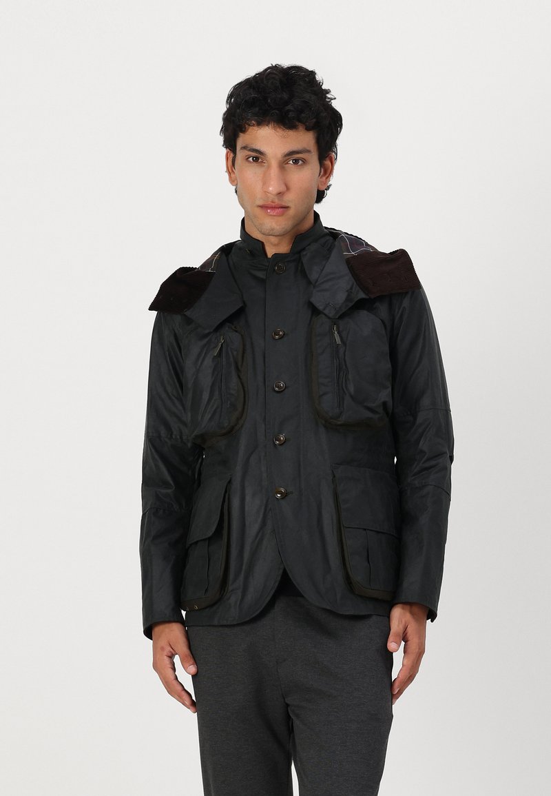 Schwarze wasserdichte Jacke mit strukturiertem Design, Corduroy-Akzenten am Kragen, Knopfverschluss und mehreren Fronttaschen.