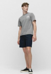 Grå bomulds t-shirt med korte ærmer og et palmetræsgrafik, parret med mørkeblå shorts og sorte sneakers med hvide såler.