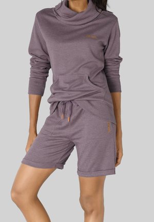 Femme portant un haut violet à manches longues assorti avec col roulé et un short à cordon avec poches avant sur fond gris.