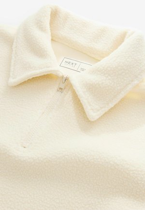 Pull en polaire blanc avec col montant, doté d'une fermeture éclair sur le devant et d'un tissu doux et texturé. L'étiquette indique "NEXT ACTIVE."