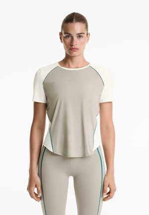 Top atletico beige leggero con maniche corte, scollatura rotonda e dettagli turchesi lungo le cuciture, abbinato a leggings aderenti coordinati.