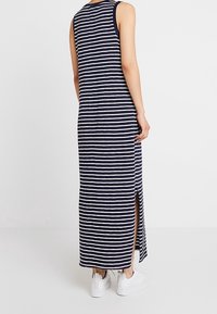 Robe longue sans manches à rayures bleu marine et blanc avec fentes latérales, en tissu léger. Associée à des baskets blanches.