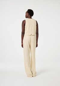 Beige Leinen-Zweiteiler, bestehend aus einem ärmellosen Oberteil und weit geschnittenen Hosen mit lockerer Passform, die eine glatte Textur und ein einfaches Design zeigen.