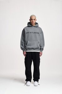 Gray hooded sweatshirt with black text "2Y STUDIOS," paired with black cargo pants and white sneakers. Simple design, relaxed fit.