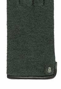 Gant en laine vert foncé, avec une surface texturée et un poignet en cuir noir décoré d'un emblème sur le côté.