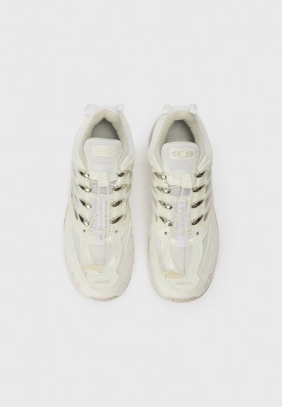 Bílé sportovní boty s síťovaným svrškem, reflexními akcenty a polstrovanou podrážkou. Obsahují výrazný systém šněrování a detaily značky.