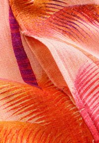 Tissu plié avec des motifs abstraits lumineux en orange, rose et violet, et des coutures visibles le long des bords.