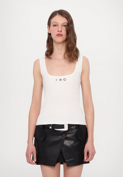 Débardeur blanc à côtes avec le logo "IRO" en noir, associé à une mini-jupe en cuir noir avec des poches à rabat et une large ceinture.