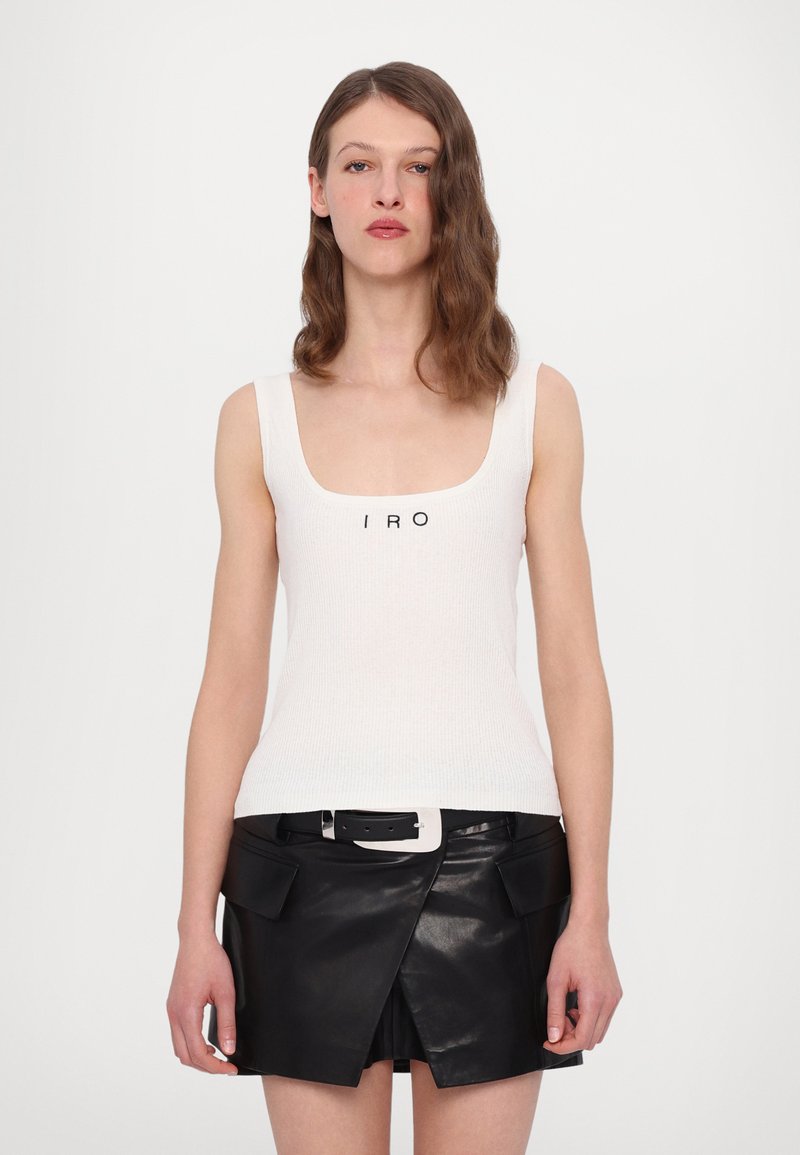 Weißes, geripptes Tanktop mit schwarzem "IRO"-Logo, kombiniert mit einem schwarzen, ledernen Minikleid mit Taschenklappen und einem breiten Gürtel.