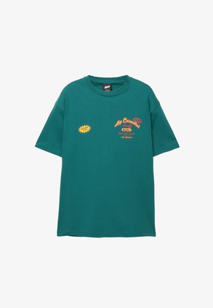 T-shirt en coton teal avec un col rond, des manches courtes et des imprimés graphiques en jaune et rouge, présentant du texte et un détail en étoile sur le devant.