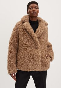 Cappotto in pelliccia sintetica marrone, con texture, dotato di ampio colletto, chiusura doppiopetto e tasche laterali; vestibilità oversize e materiale morbido e riccio.