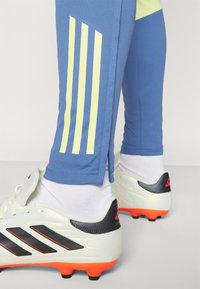 Blue athletic pants with yellow stripes, designed with a tapered fit. White soccer cleats feature black and red accents.