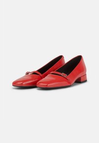 Bailarinas rojas de charol con punta afilada, que cuentan con una tira frontal con una pequeña hebilla metálica y un tacón bajo tipo bloque.