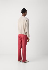 Pull beige texturé à coupe décontractée, associé à un pantalon rose à jambes droites. La tenue est complétée par des chaussures minimalistes de couleur claire.