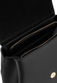 Black leather bag with a gold zip closure, featuring multiple compartments inside and a rounded base. Soft texture with a smooth finish.