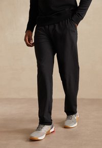 Svarta träningsbyxor med en avslappnad passform och elastisk midja. Matcher med grå sneakers som har röda accenter och en strukturerad ovandel.
