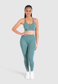 Conjunto atlético en tono verde azulado con un sujetador deportivo ajustado y acanalado, y leggings de cintura alta, ambos en una tela suave y elástica. Presenta una textura suave.
