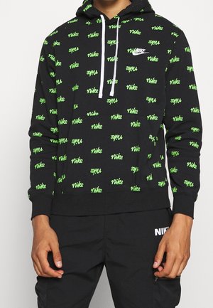 Zwarte Nike-trui met een herhaald groen logo en witte trekkoorden, gedragen met zwarte Nike-broek met een wit logo.