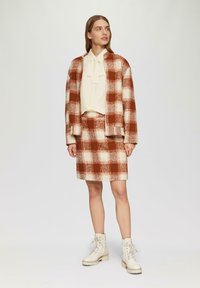 Rood en crèmetje geblokte gebreide cardigan en rokset met een strikblouse. Witte veterschoenen met een dikke zool maken de look compleet.