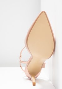 Chaussure à talon haut en suede rose avec un bout pointu, une fine bride de cheville et un talon effilé. Semelle beige lisse avec texture nervurée.