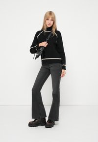 Melna džemperis ar baltām akcentiem, augsts kakls un garas piedurknes. Apvienots ar pelēkiem platajiem džinsiem un masīvām melnām platformām.