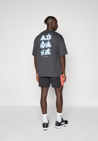 T-shirt gris surdimensionnée avec un texte graphique coloré dans le dos, associée à un short noir et des baskets noires avec des rayures blanches.