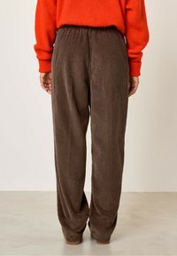 Rjave kordurojske hlače z ohlapnim krojem, ki imajo strukturiran grimkasti vzorec in elastičen pas. Tkanina ima mehak, puhast videz.