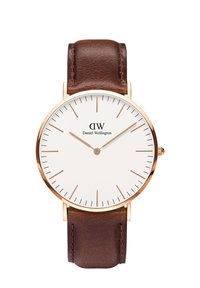 Brunt läderremmsklocka med en vit urtavla. Har en minimalistisk design, guldfärgade accenter och tunna timmarkörer med en liten krona.