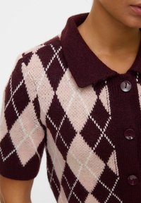 Pull en maille à manches courtes dans un motif argyle bordeaux et rose clair, avec un col et de boutons foncés. Texture douce.