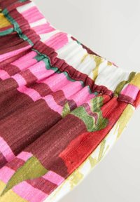 Gros plan sur un tissu avec une ceinture élastique présentant des rayures verticales en rose, rouge, vert, jaune et blanc avec un motif tricoté texturé.
