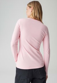 Hellrosa langärmliges Oberteil aus weichem Stoff. Mit rundem Ausschnitt und figurbetontem Design, glatter Textur und ohne sichtbare Muster.