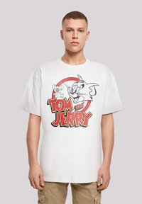 Hvid bomulds T-shirt med et grafisk motiv af Tom og Jerry. Designet inkluderer fed rød og sort tekst med tegneseriemotiver af en kat og en mus.