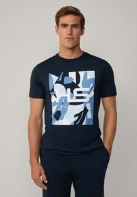 Navy blauwe katoenen t-shirt met een grote grafische afbeelding in tinten blauw en zwart met de tekst "HACKETT", korte mouwen en een ronde halslijn.