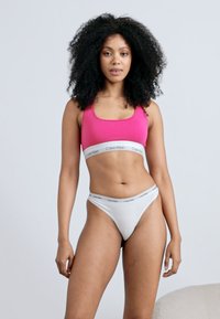 Ροζ κοντό τοπ με λευκή λωρίδα λογότυπου Calvin Klein, σε συνδυασμό με λευκή ταντ φανέλα που διαθέτει παρόμοια λωρίδα λογότυπου. Λείο υφασμάτινο σχέδιο.