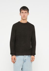 Donker gebreid trui met een ronde hals, textuurstof, en geribde mouw- en onderranden, gecombineerd met lichtblauwe jeans.