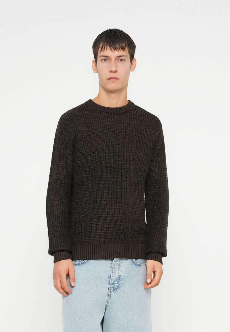 Donker gebreid trui met een ronde hals, textuurstof, en geribde mouw- en onderranden, gecombineerd met lichtblauwe jeans.