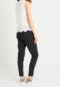 Top bianco senza maniche con dettagli ad occhiello scallop, abbinato a pantaloni tapered a righe bianche e nere e sneakers bianche con strappi a fantasia.