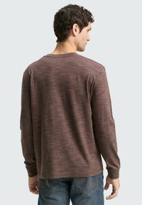 Langsleeve shirt van een gestructureerd, donkerbruin materiaal met subtiele lichte stippen. Ronde halslijn en een relaxte fit, gecombineerd met blauwe jeans.