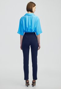 Světle modrá blůza s krátkým rukávem a límcem, spárovaná s tmavě modrými kalhotami s vysokým pasem. Slim fit, hladká textura a žádné viditelné vzory nebo kovové prvky.