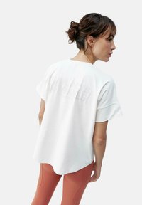 Balta trumpa rankovėmis marška su apvalia apačia ir tekstūruotu nugaros spaudiniu. Sujungta su prigludusiomis, aukštu liemeniu, rūdžių spalvos leggingais.