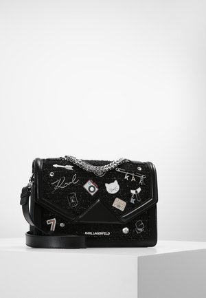 Schwarze Karl Lagerfeld Tasche mit silberner Kette, verschiedene Emaille-Pins darunter eine Katze, eine Kamera, ein Pfeil, eine Sicherheitsnadel und Logodetails.