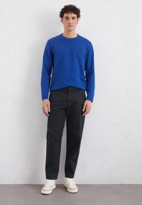 Blauer Langarm-Pullover mit Rundhalsausschnitt kombiniert mit schwarzen Hosen und weißen Sneakers, mit einem figurbetonten Design und einfarbigem Stoff.