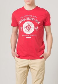 Rotes Baumwoll-T-Shirt mit grafischem Design "Sahara Desert Run", rundem Emblem und Text. Kurze Ärmel, runder Ausschnitt.