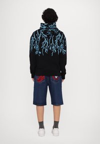 Black hoodie with blue lightning pattern, paired with denim shorts featuring red accents and white sneakers. Wool socks visible.