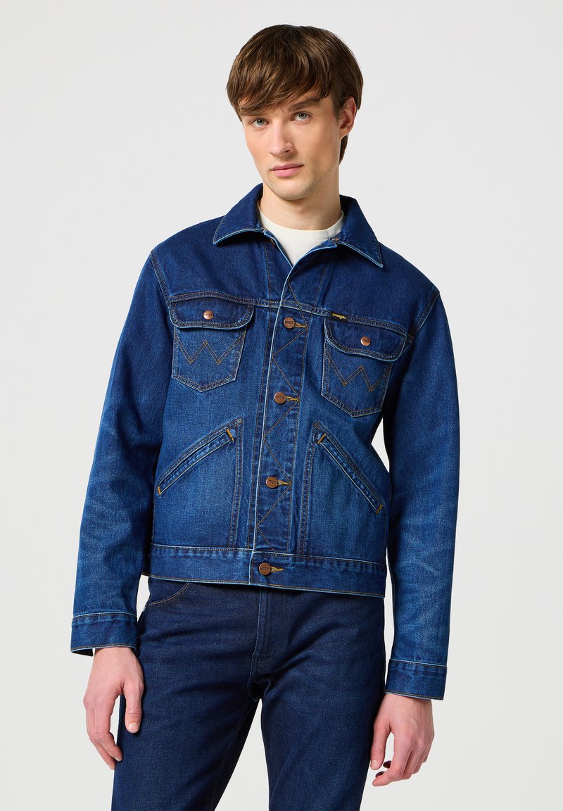 Modrá džínsová bunda klasického střihu, která má dvě náprsní kapsy, kovové knoflíky a kontrastní švy. Nosit s odpovídajícími džíny.