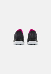 Schwarze Sportschuhe mit strukturiertem Finish, ausgestattet mit einem pinken Innenfutter, weißen Sohle und abgerundetem Absatz. Keine sichtbaren Schnürsenkel oder Beschläge.