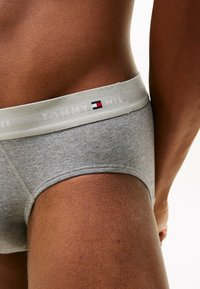 Culotte en coton grise avec une ceinture élastique gris clair arborant le logo "TOMMY HILFIGER" et un petit accent de logo en rouge, blanc et bleu.